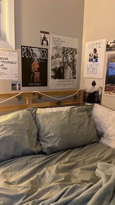 an unmade bed in a room with posters on the wall and pictures above it