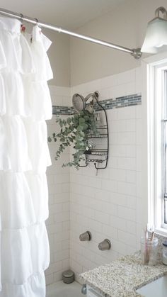 a white shower curtain in a bathroom next to a sink and bathtub with plants on it