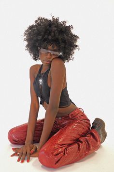 a woman sitting on the ground with her legs crossed and wearing shiny red leggings