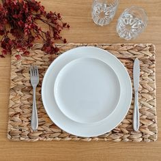 a place setting with white plates, silverware and red flowers on a woven place mat