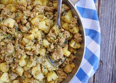 a bowl filled with meat and potatoes on top of a blue and white checkered cloth