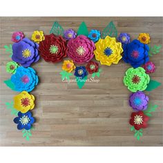 colorful paper flowers arranged in the shape of a heart on a wooden floor with green leaves