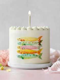 a birthday cake decorated with colorful fish on top of a white plate and lit candles