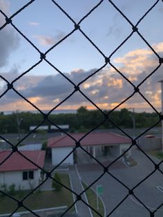 the view from behind a chain link fence at a parking lot with houses in the background