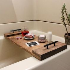 a bath tub with a wooden tray on the side holding soap, candles and other items