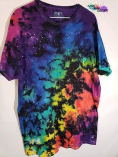 a t - shirt that is multicolored with stars and clouds on it, sitting on a hanger