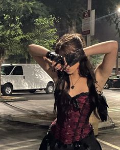 a woman in a corset with her hands on her head and holding a camera