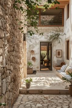 an alley way with stone walls and potted plants on either side, leading to the front door