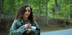 a woman is holding a drink and looking at the camera while standing in the street