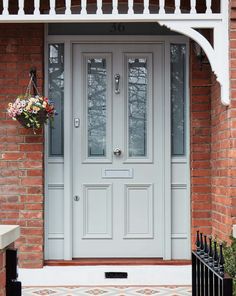 a grey front door with glass panels and wrought iron railing on the side of a brick building