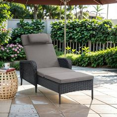 an outdoor lounge chair with an umbrella in the middle of a patio area next to some bushes