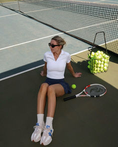 a woman sitting on the ground with tennis racket and ball in front of her