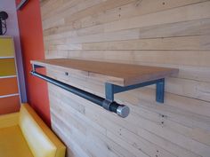 a wooden wall with metal brackets on it and a yellow chair in the corner next to it