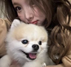 a woman holding a small white dog in her arms with long brown hair and blue eyes