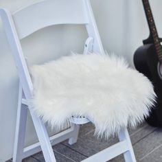 a white chair with a furry seat pad next to an acoustic guitar on the floor