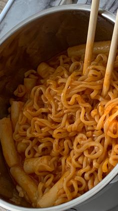 two wooden chopsticks sticking out of noodles in a pot