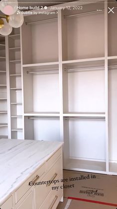 an empty closet with white shelves and marble counter top in the middle, next to a window