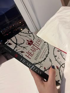 a person holding a book in their hand on top of a bed with white sheets