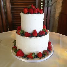 a three tiered cake with strawberries and blueberries on the top is sitting on a table