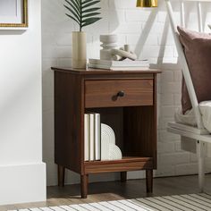 a nightstand with books on it next to a white chair and wall in the background