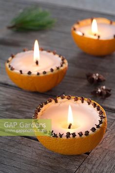 three oranges with candles in them sitting on a wooden table next to pine cones