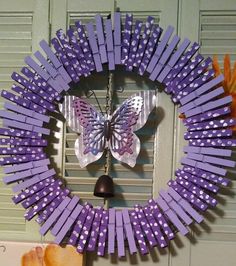 a wreath made out of purple sticks with a butterfly on it and a bell hanging from the front