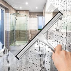 a hand holding a brush in front of a bathroom window with water drops on it