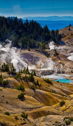 steam rises from the ground in front of trees and blue water on a sunny day