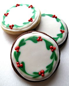 three decorated cookies sitting next to each other on top of a white tablecloth with red and green decorations