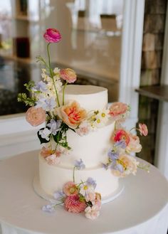 a three tiered white cake with flowers on the top and bottom is sitting on a table