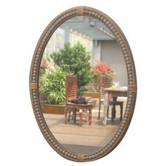 an oval mirror with rope trim around the edges shows a dining room table and chairs