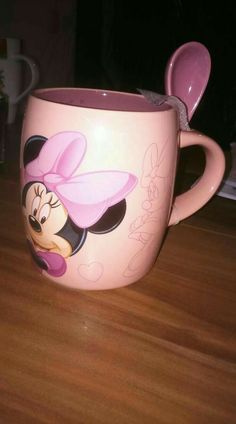 a pink mickey mouse mug with a spoon in it's mouth on a wooden table