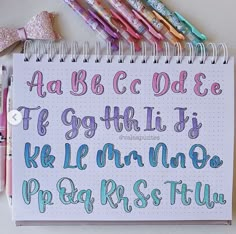 a notebook with some writing on it next to markers and pens that spell out the alphabet