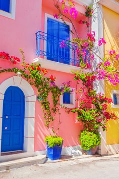 a pink building with blue doors and flowers on the outside, in front of it