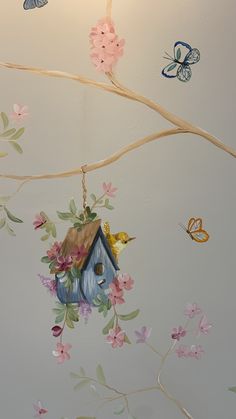 a birdhouse hanging from a tree branch with flowers and butterflies painted on the wall