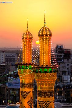 two large towers with lights on them in the middle of a city at sunset or dawn