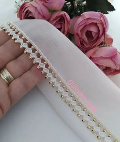 a hand is holding a white ribbon with gold rivets on it and pink roses in the background