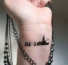 a woman's wrist with a small city tattoo on her left arm and a chain around the wrist