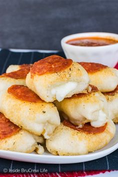 a white plate topped with mini pizzas next to a bowl of tomato sauce and a cup of soup