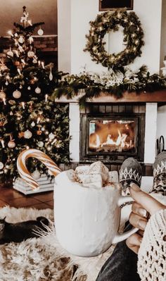 a person holding a mug in front of a fireplace with christmas decorations on the mantle