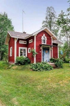 a red house with white trim and blue door is in the middle of green grass