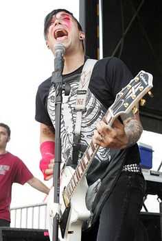 a man singing into a microphone while holding a guitar in front of him and another person standing behind him