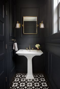 a bathroom with black walls and white sink in the center, gold mirror on the wall