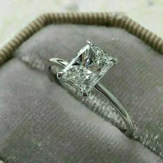 a princess cut diamond ring sitting on top of a cushioned velvet case in a box