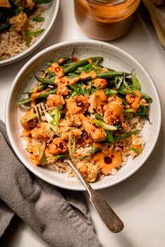 a white plate topped with chicken and veggies covered in sauce next to rice