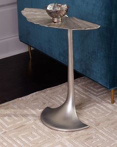 a metal table with a flower on it in front of a blue couch and rug