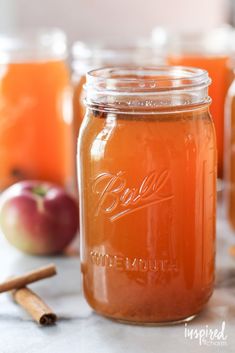 three jars filled with liquid sitting on top of a table next to apples and cinnamon sticks