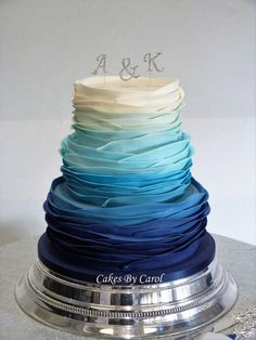 a wedding cake with blue, white and green layers is displayed on a silver platter