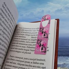 an open book with a pink tag attached to it's cover next to the ocean