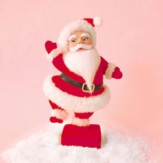 a santa clause figurine standing on top of some white snow in front of a pink background